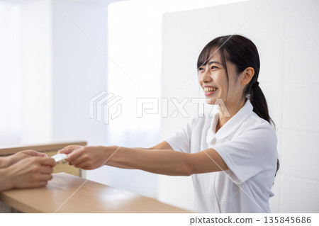A woman in a white coat receiving a card at the reception 135845686