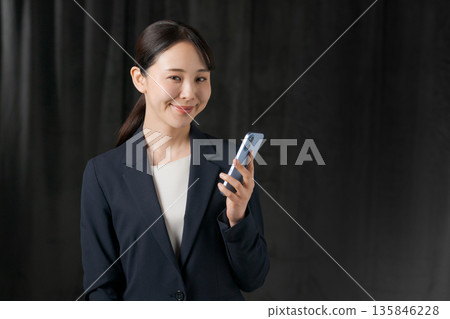 A woman in a suit holding a smartphone (black background) 135846228