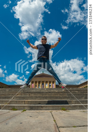 A man in a blue shirt is jumping on a set of stairs in front of a building. Philadelphia Museum of Art A man in a blue shirt is jumping on a set of stairs in front of a building. Philadelphia Museum of Art 135846234