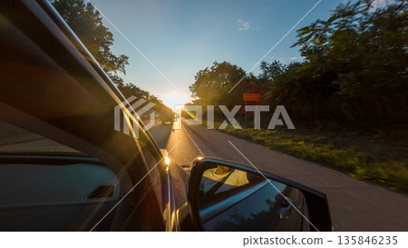 A car is driving down a road with a sunset in the background A car is driving down a road with a sunset in the background 135846235