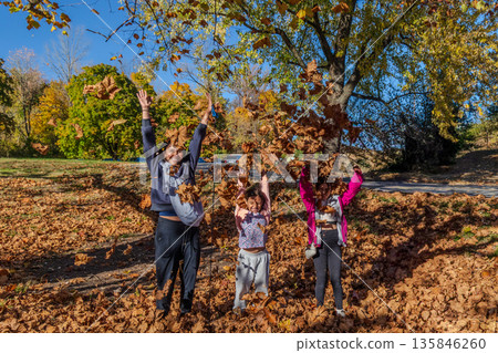 A family of three is playing in the leaves, with the father holding a baby A family of three is playing in the leaves, with the father holding a baby 135846260