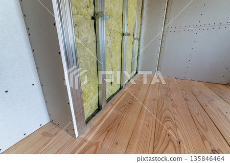 Wall of a room under renovation with mineral rock wool insulation and metal frame prepared for drywall plates. 135846464