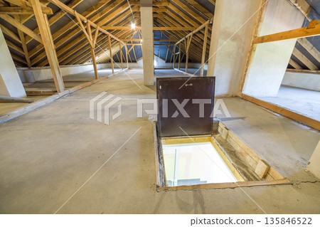 Attic of a building with wooden beams of a roof structure and a fire exit door in floor. 135846522