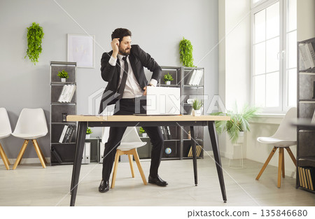 Cheerful businessman dancing by desk with laptop in light contemporary office 135846680