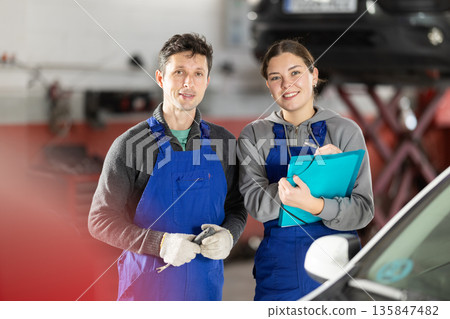 Young woman supervisor manager of car repair station with papers listens to male master Young woman supervisor manager of car repair station with papers listens to male master 135847482