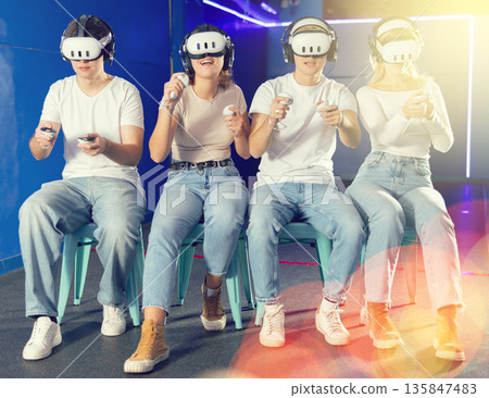 In darkened hall of gaming club, four friends in VR helmet takes part in group game In darkened hall of gaming club, four friends in VR helmet takes part in group game 135847483