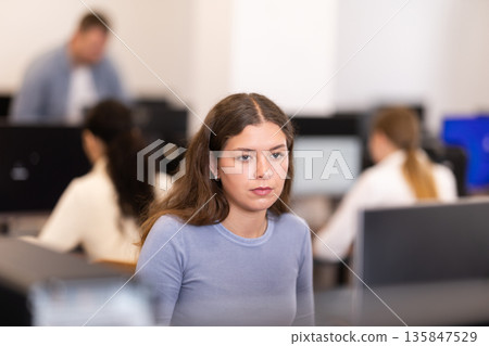 Young woman student of computer courses looks at monitor screen, types on keyboard and does work Young woman student of computer courses looks at monitor screen, types on keyboard and does work 135847529