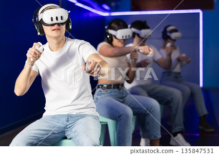 In darkened hall of gaming club, guy in VR helmet takes part in group game In darkened hall of gaming club, guy in VR helmet takes part in group game 135847531