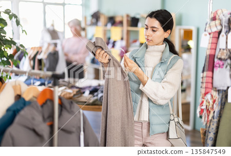 Armenian woman holding woolen pants in her hands against the background of the interior of a shop 135847549