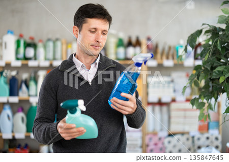 Among shop windows, man buyer leisurely examines goods and chooses glass cleaner spray Among shop windows, man buyer leisurely examines goods and chooses glass cleaner spray 135847645