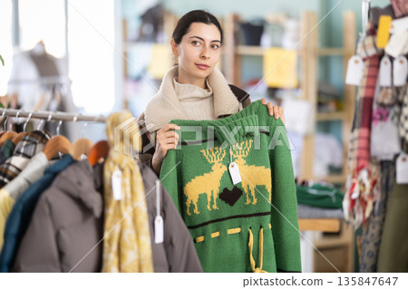Girl chooses fashionable sweater in clothing store Girl chooses fashionable sweater in clothing store 135847647