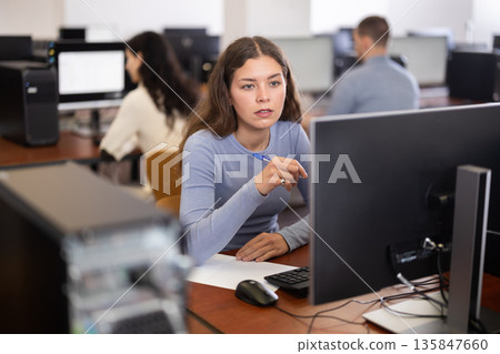 Female student looks at monitor screen, write down note in notebook 135847660