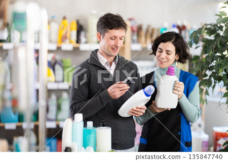 Woman seller help man visitor scan QR code, get information about laundry conditioner in mobile app Woman seller help man visitor scan QR code, get information about laundry conditioner in mobile app 135847740