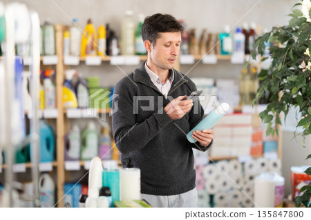 Middle-aged man scanning QR-code on shampoo at department store 135847800