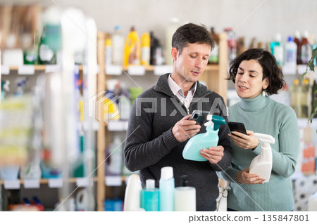 Female salesperson offers to buy a spray glass cleaner while a man checks a QR code using smartphone 135847801