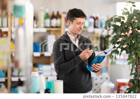 man in a jumper stands in the household chemicals department of a supermarket and scans the barcode man in a jumper stands in the household chemicals department of a supermarket and scans the barcode 135847822