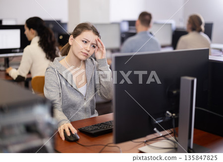 Young woman student of computer courses looks at monitor screen, types on keyboard and does work 135847825