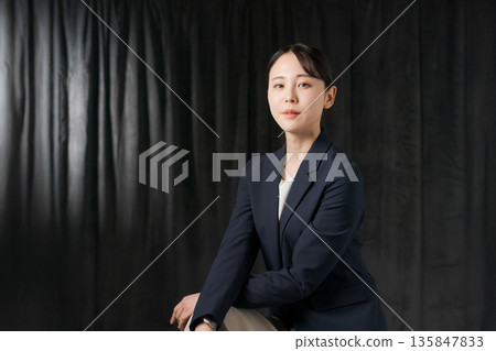 一位身穿西裝的女子站在黑色窗簾前 一位身穿西裝的女子站在黑色窗簾前 135847833