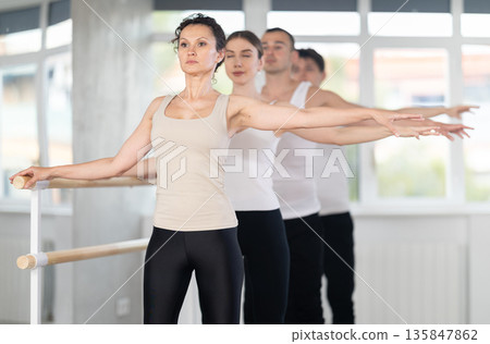 Fit woman mastering second position at barre in ballet studio Fit woman mastering second position at barre in ballet studio 135847862