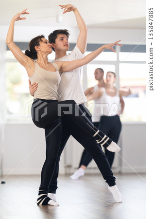 Happy smiling woman dressed in black and white sportswear enjoying ballet choreography with male partner during group class in dance salon Happy smiling woman dressed in black and white sportswear enjoying ballet choreography with male partner during group class in dance salon 135847885