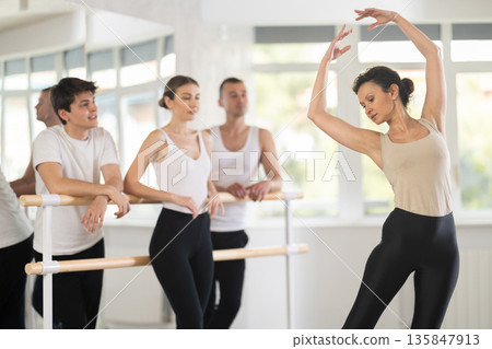 Female ballet teacher showing movements to students in studio Female ballet teacher showing movements to students in studio 135847913
