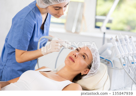Young woman cosmetologist doing cleansing procedure to young woman 135847939