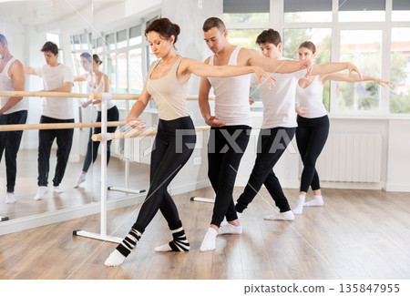 Woman performing demi rond at ballet barre in group studio 135847955