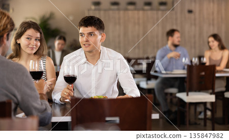 Couple and adult man eating and talking in restaurant Couple and adult man eating and talking in restaurant 135847982