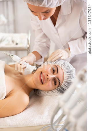 Female client undergoing anti-aging ultrasonic phonophoresis procedure on face 135847984