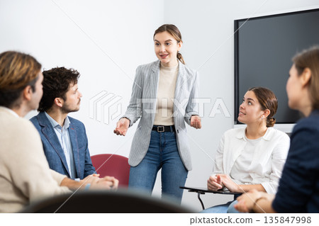 Young female teacher listening to answers from students of different ages while they sitting in circle at foreign language lesson Young female teacher listening to answers from students of different ages while they sitting in circle at foreign language lesson 135847998