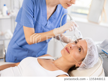 Young woman cosmetologist doing whitening procedure to young woman Young woman cosmetologist doing whitening procedure to young woman 135848011