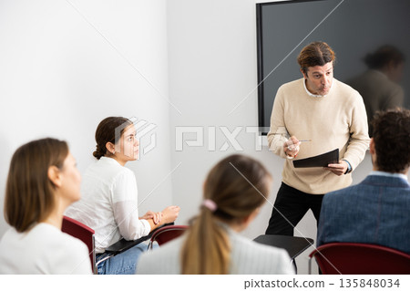 Competent male tutor teaching students in college classroom 135848034