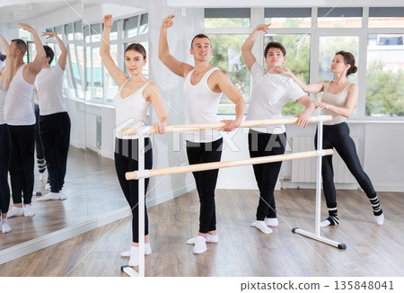 Experience female ballet instructor adjusting students form. Diligent girls and boys practice ballet movements near ballet barre in dancing hall 135848041