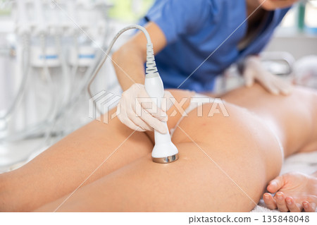Aesthetician administering high frequency ultrasound procedure on buttocks of female patient 135848048