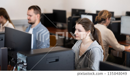 Young woman student of computer courses looks at monitor screen, types on keyboard and does work 135848049