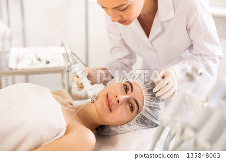 Young woman cosmetologist doing microcurrent procedure to young woman Young woman cosmetologist doing microcurrent procedure to young woman 135848063