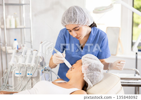 Female aesthetician performing radiofrequency facial skin tightening procedure on woman Female aesthetician performing radiofrequency facial skin tightening procedure on woman 135848092