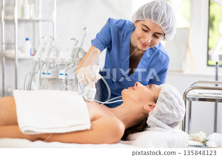 Female cosmetologist performing procedure on decollete area to woman using cooling attachment Female cosmetologist performing procedure on decollete area to woman using cooling attachment 135848123