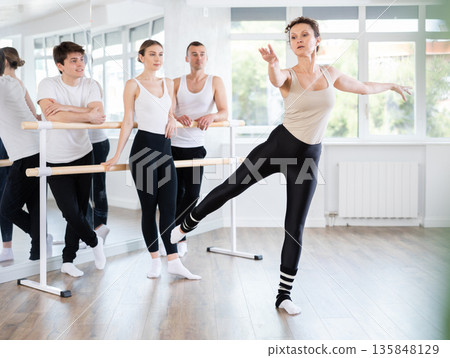 Female ballet teacher showing movements to students in studio Female ballet teacher showing movements to students in studio 135848129