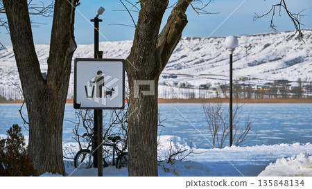 A clean up after your pet sign stands before a frozen lake and snowy mountains in winter 135848134