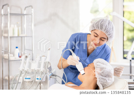 Female cosmetologist performing facial cleansing with ultrasonic shovel on woman 135848135