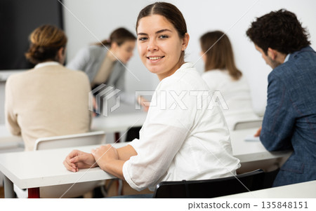Portrait of smiling young woman smiling at camera during studying of foreign language with group of students in class 135848151