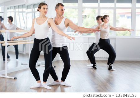 Positive ballet dancers couple performing graceful choreography, training demi plie ballet pose in gym or ballet hall 135848153