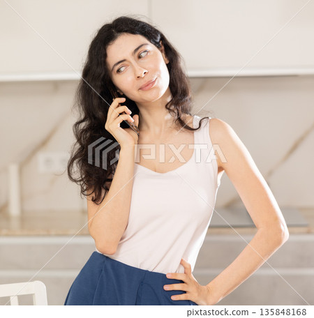 Young woman talking on phone in kitchen Young woman talking on phone in kitchen 135848168