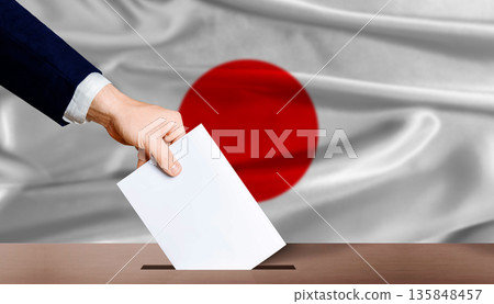Japan presidential vote 2026. Hand placing a ballot in ballot box with the Japanese flag in the background Japan presidential vote 2026. Hand placing a ballot in ballot box with the Japanese flag in the background 135848457