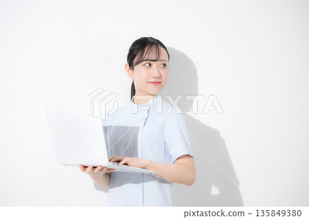 A nurse wearing a light blue nurse uniform and holding a computer. Image of job change, recruitment, etc. White background 135849380