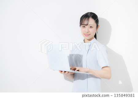 A nurse wearing a light blue nurse uniform and holding a computer. Image of job change, recruitment, etc. White background 135849381