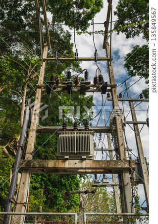 High voltage power transformer and utility poles with electrical cables in tropical forest setting on Koh Samui Thailand under blue sky 135849567