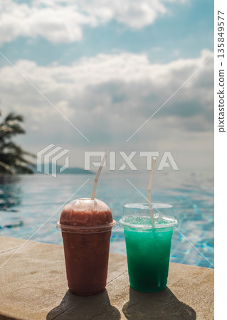 Two colorful cold drinks on pool edge with ocean horizon and soft cloudy sky creating tropical vacation refreshment scene with wide copy space for travel and resort concepts 135849577