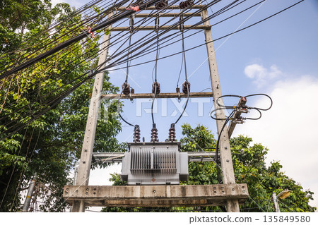 Electrical transformer and power lines on concrete utility frame in tropical Thailand, green trees and clear sky background Electrical transformer and power lines on concrete utility frame in tropical Thailand, green trees and clear sky background 135849580